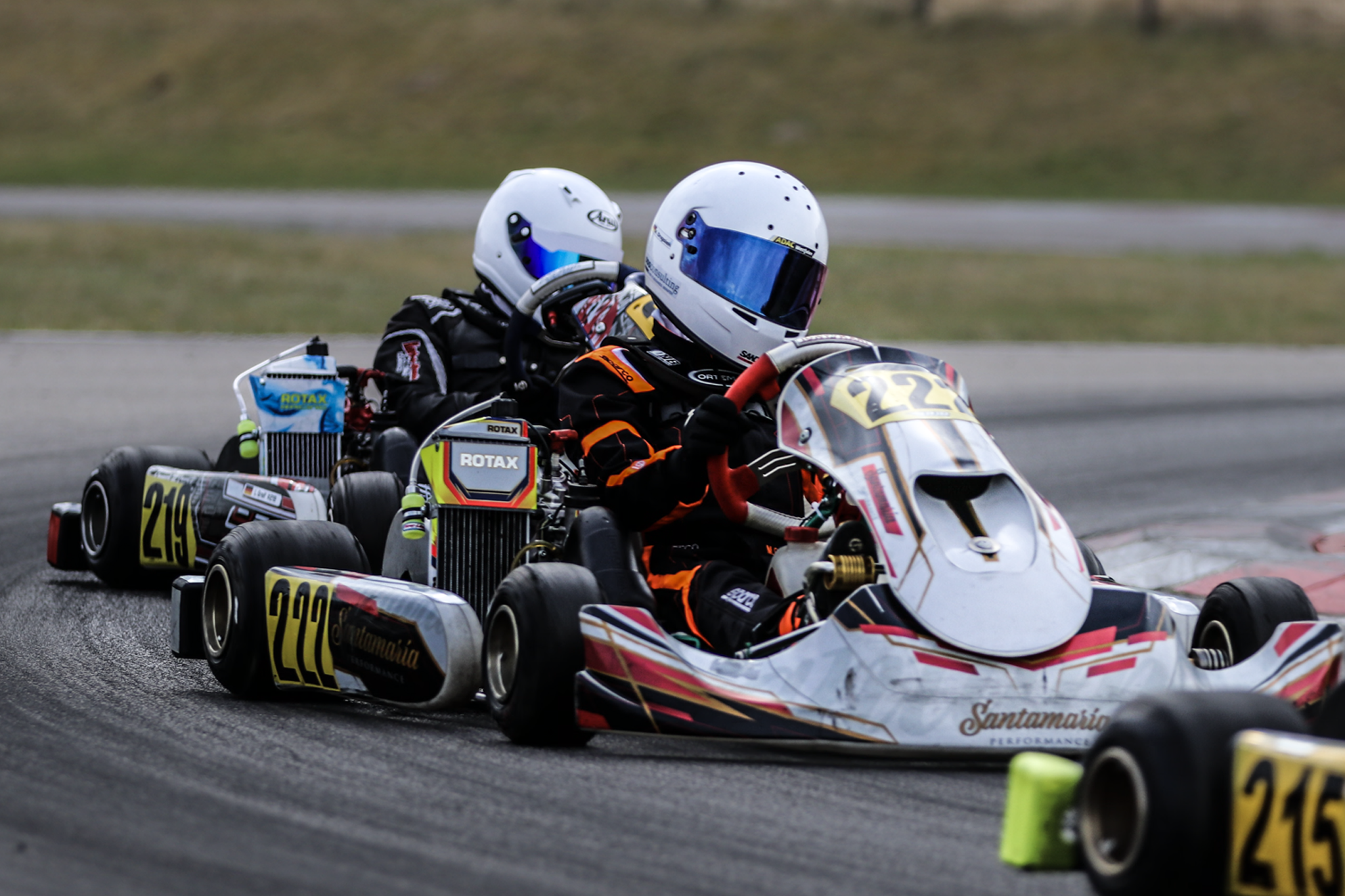 Max Ongsiek im Go-Kart mit der Startnummer 228, unterwegs in einer Kurve auf der Rennstrecke. Ausgestattet mit ROTAX-Motor, weißem Helm und schwarzem Rennanzug mit orangefarbenen Streifen.
